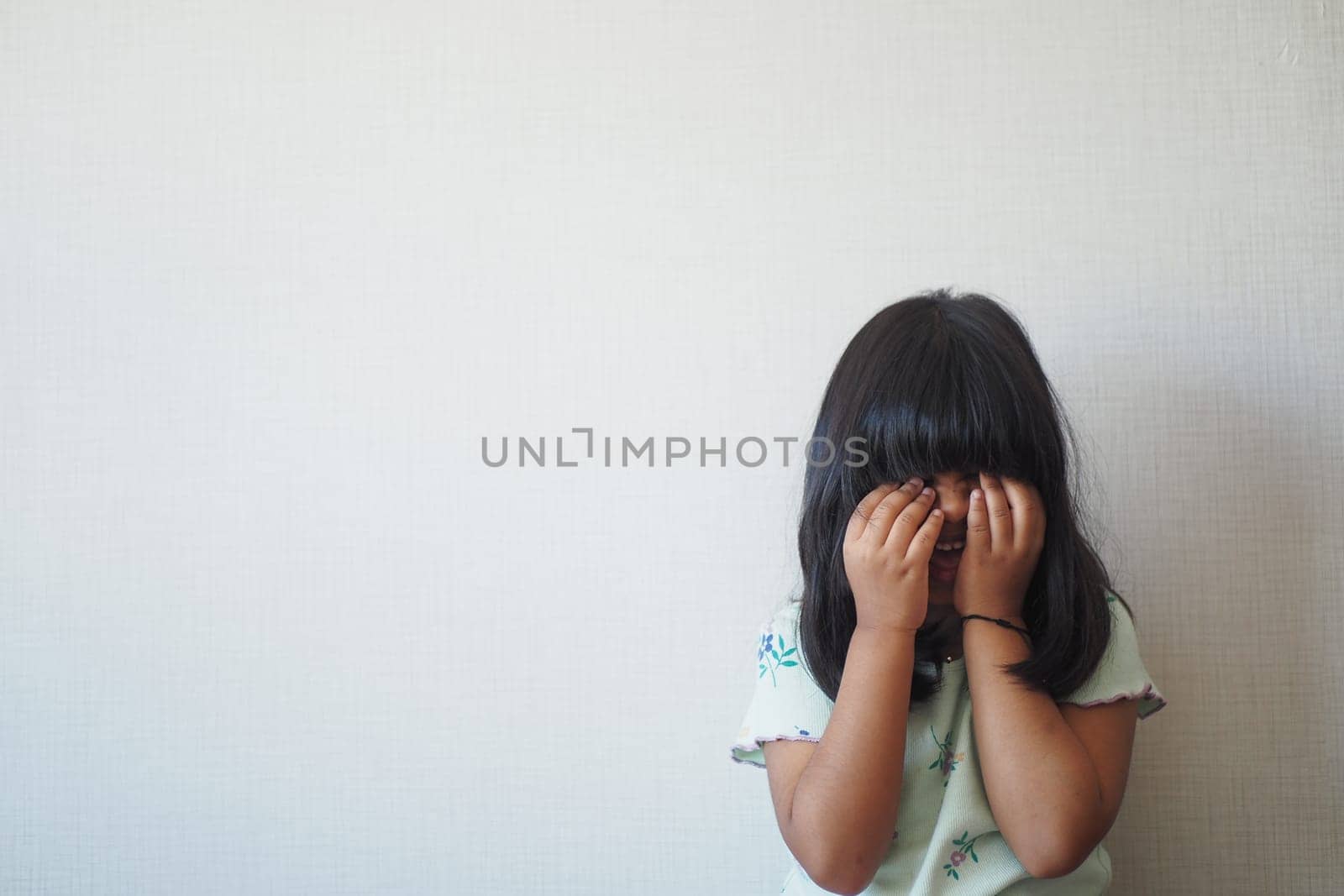 a upset child girl cover her face with hand .