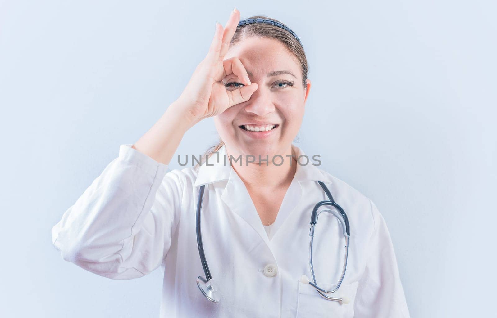 Young female doctor approving with finger on isolated background. Cheerful female doctor gesturing approval isolated