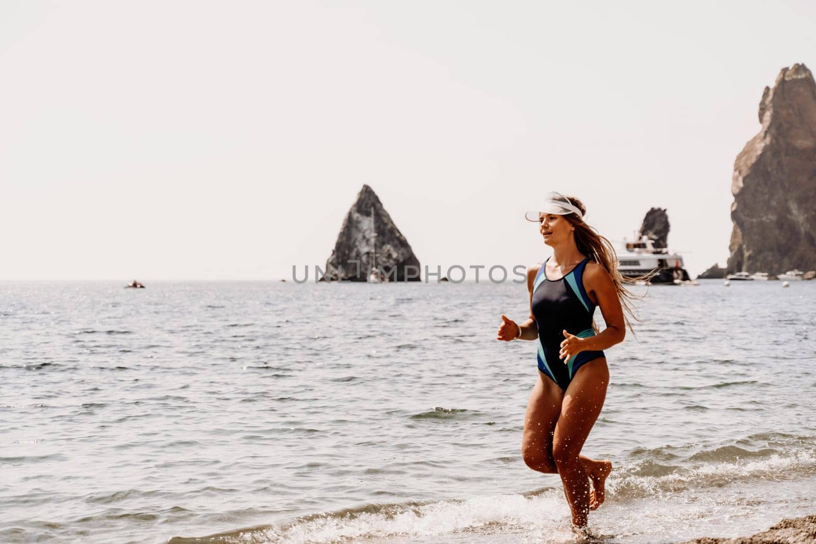 Woman beach vacation photo. A happy tourist in a blue bikini enjoying the scenic view of the sea and volcanic mountains while taking pictures to capture the memories of her travel adventure