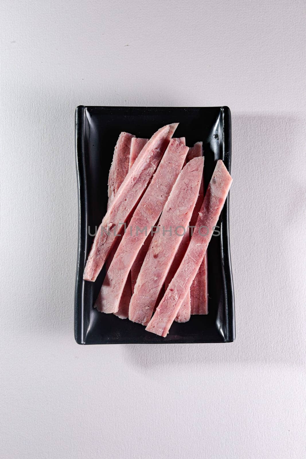 sliced boiled meat on a black plate on a white background, top view by tewolf