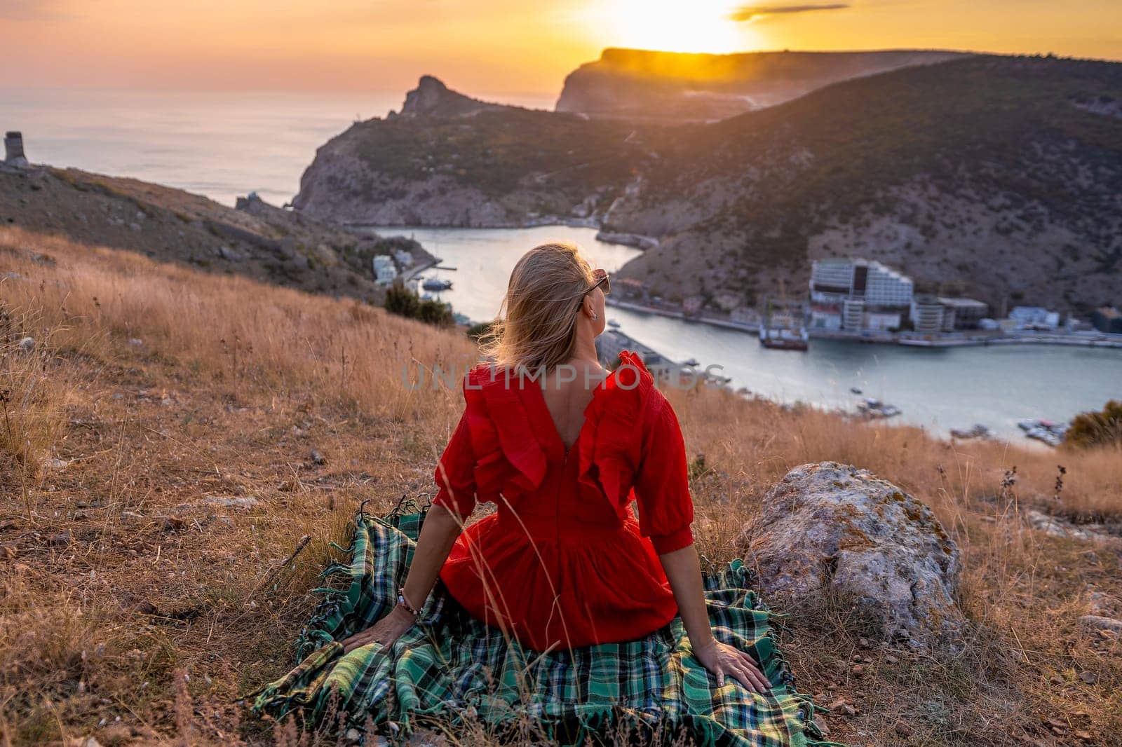 Woman sunset sea mountains. Happy woman siting with her back on the sunset in nature summer posing with mountains on sunset, silhouette. Woman in the mountains red dress, eco friendly, summer landscape active rest.