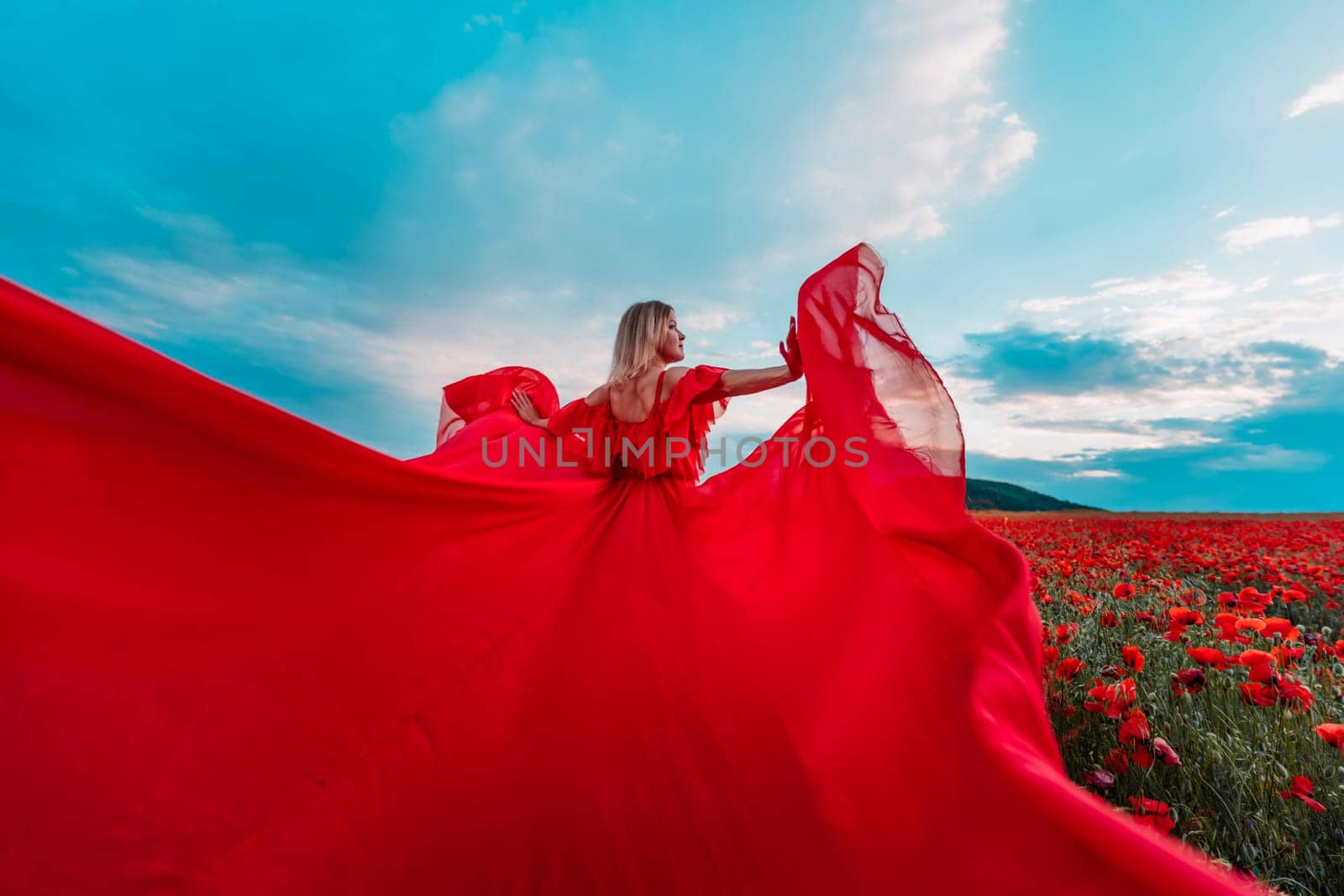 Woman poppy field red dress. Happy woman in a long red dress in a beautiful large poppy field. Blond stands with her back posing on a large field of red poppie