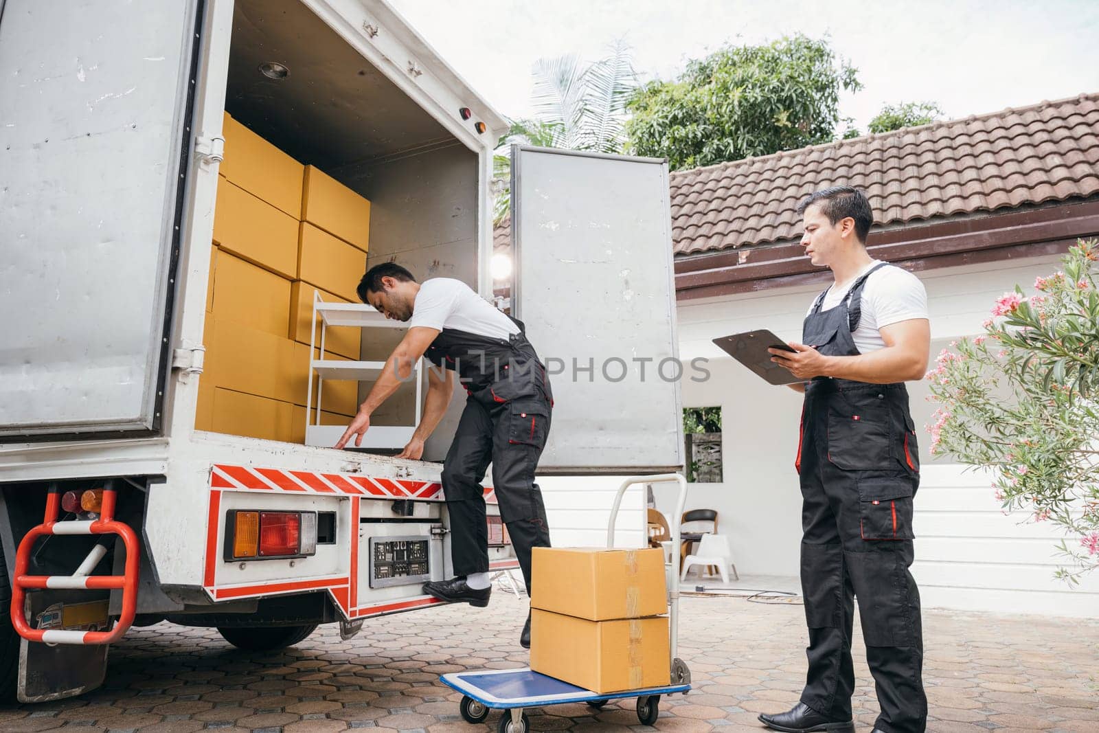 Uniformed removal company workers unload boxes and furniture from the truck exhibiting excellent teamwork. Their dedication guarantees a smooth move into the new home ensuring happiness. Moving Day by Sorapop