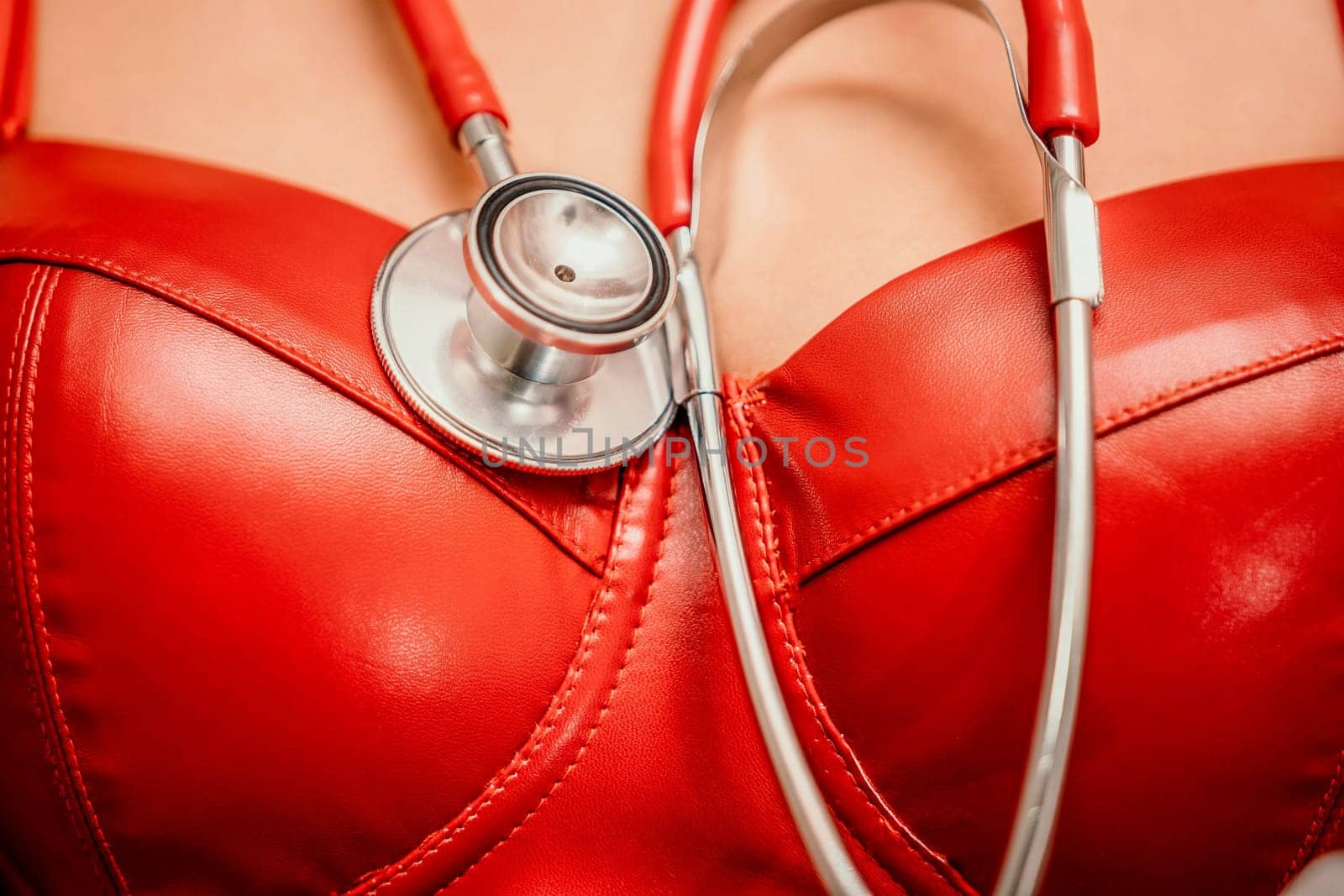 Young woman in red corset and black leather pants with a phonendoscope. Sexy brunette nurse in red and black costume with a stethoscope in her hands. Role doctor play. Entertainment