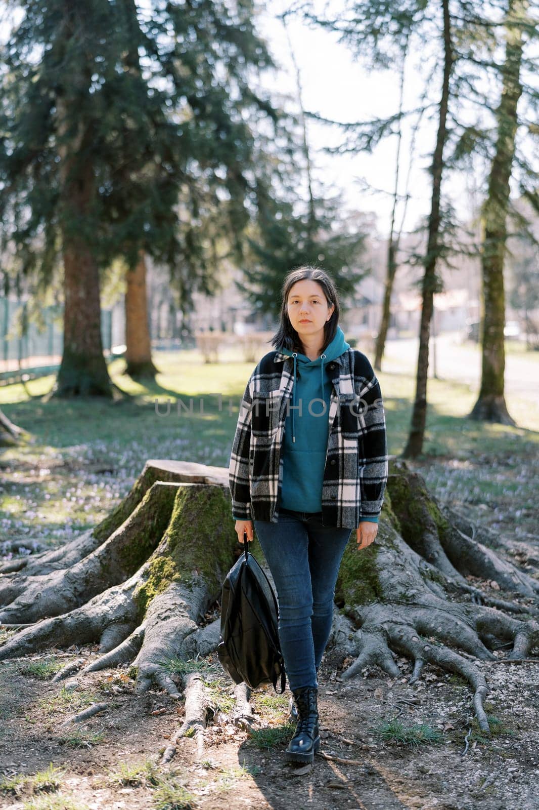 Young woman with a backpack in her hand walks near a huge stump in the forest. High quality photo