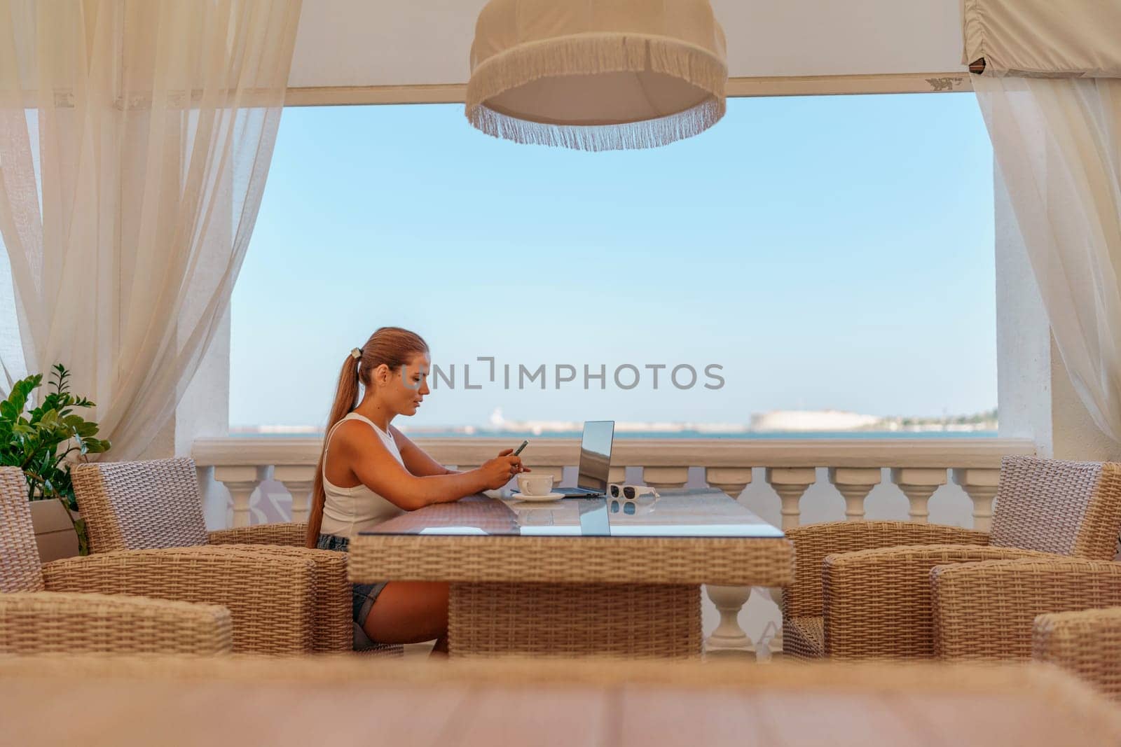 Woman coffee cafe laptop sea. Modern businessman in white uniform working on laptop in coffee shop. Woman sitting at a coffee shop with mobile phone drinking coffee. by Matiunina