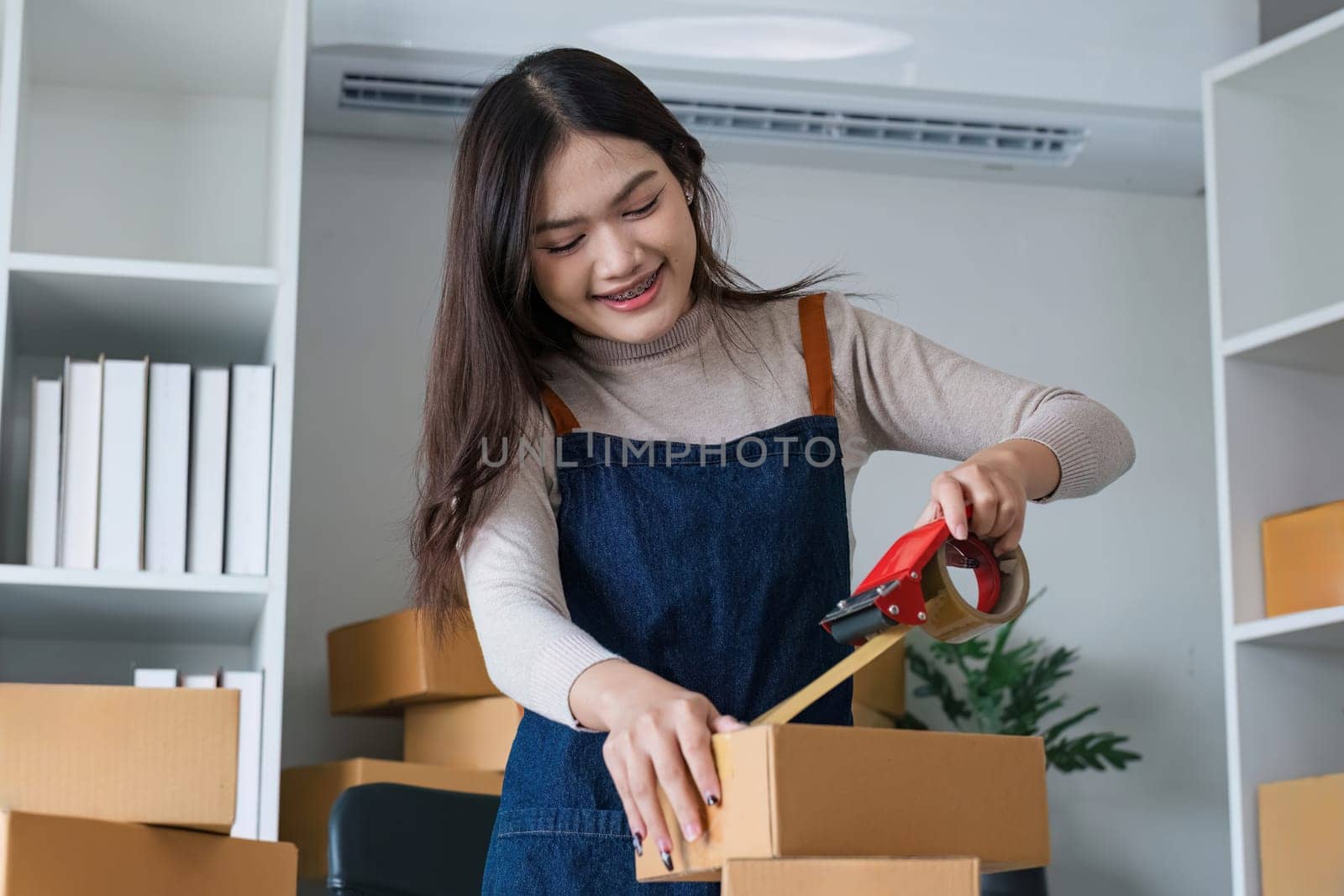 Young asian woman taping up a cardboard box in home office SME e-commerce business, relocation and new small business concept, SME concept.