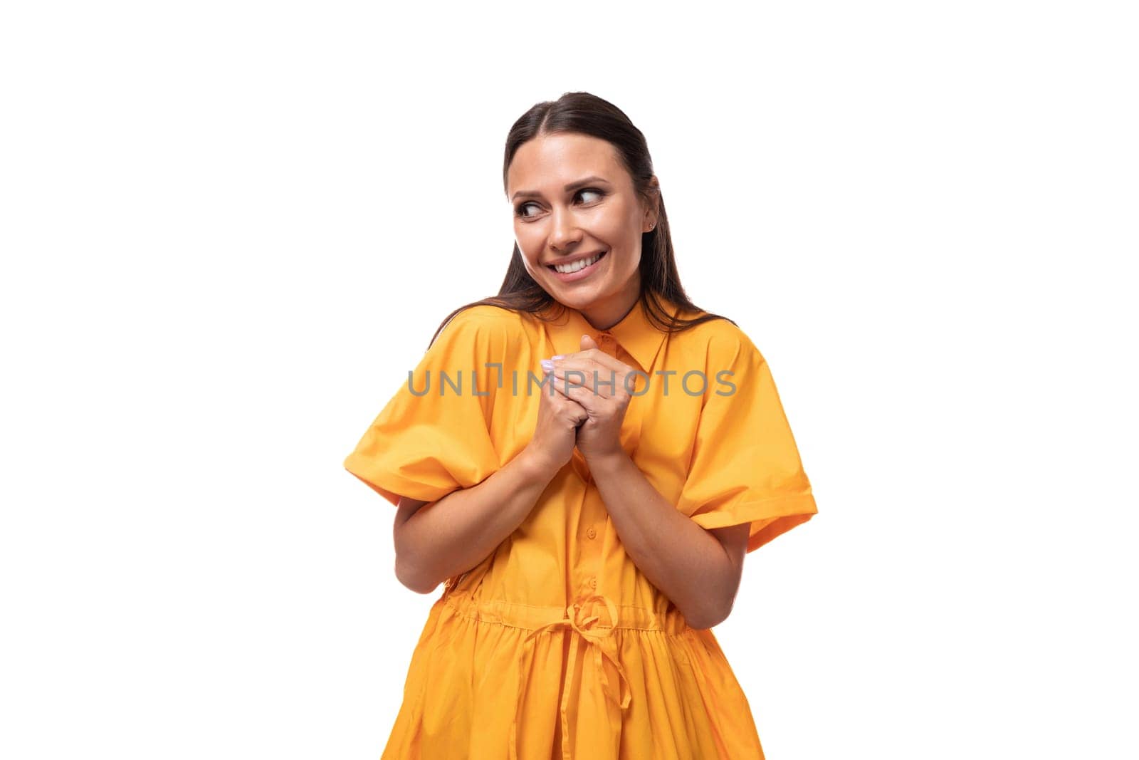 European young woman with black hair dressed in an orange summer dress smiling shyly looking away by TRMK