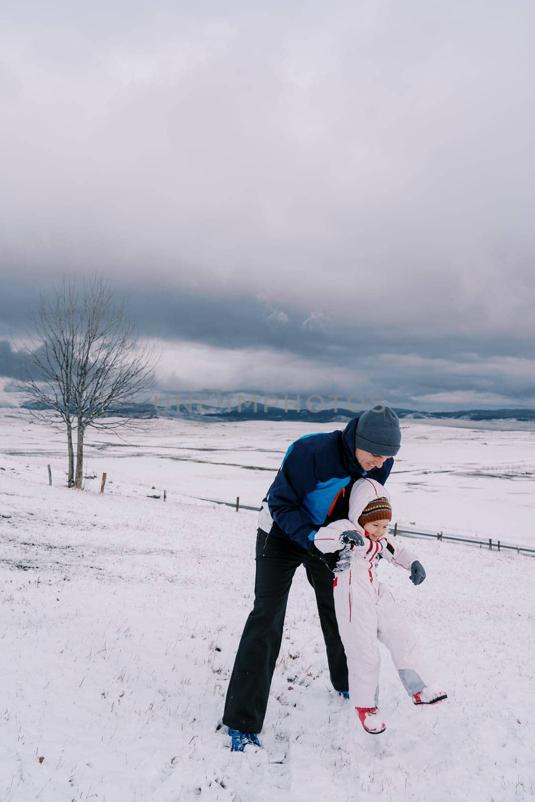 Dad lifts a laughing little girl while standing on a snowy slope. High quality photo