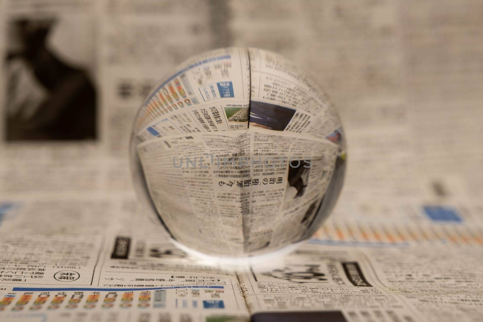 A glass globe reveals the letters inside, with a newspaper in the background. by TEERASAK