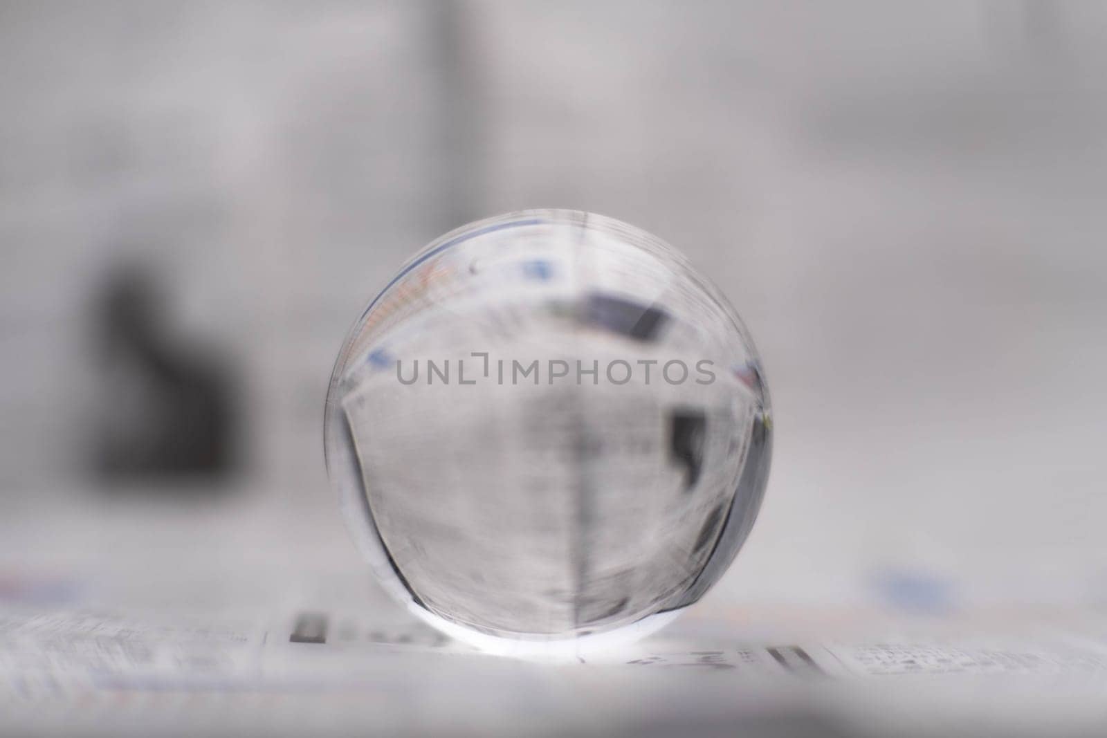 A glass globe reveals the letters inside, with a newspaper in the background. by TEERASAK