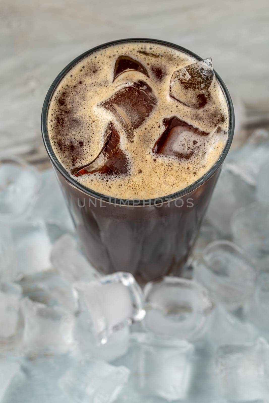 A cup of Iced Americano Coffee with ice cubes placed on a wooden table in a coffee shop. Top view of a glass of coffee. by Sonat