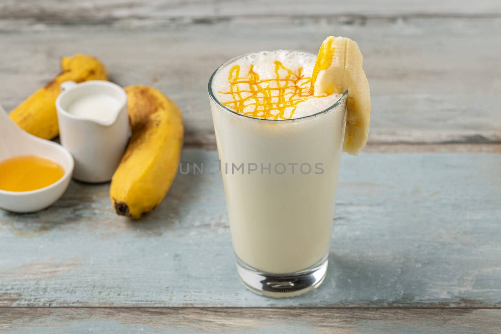 Milk with honey and banana in glass glass on wooden table