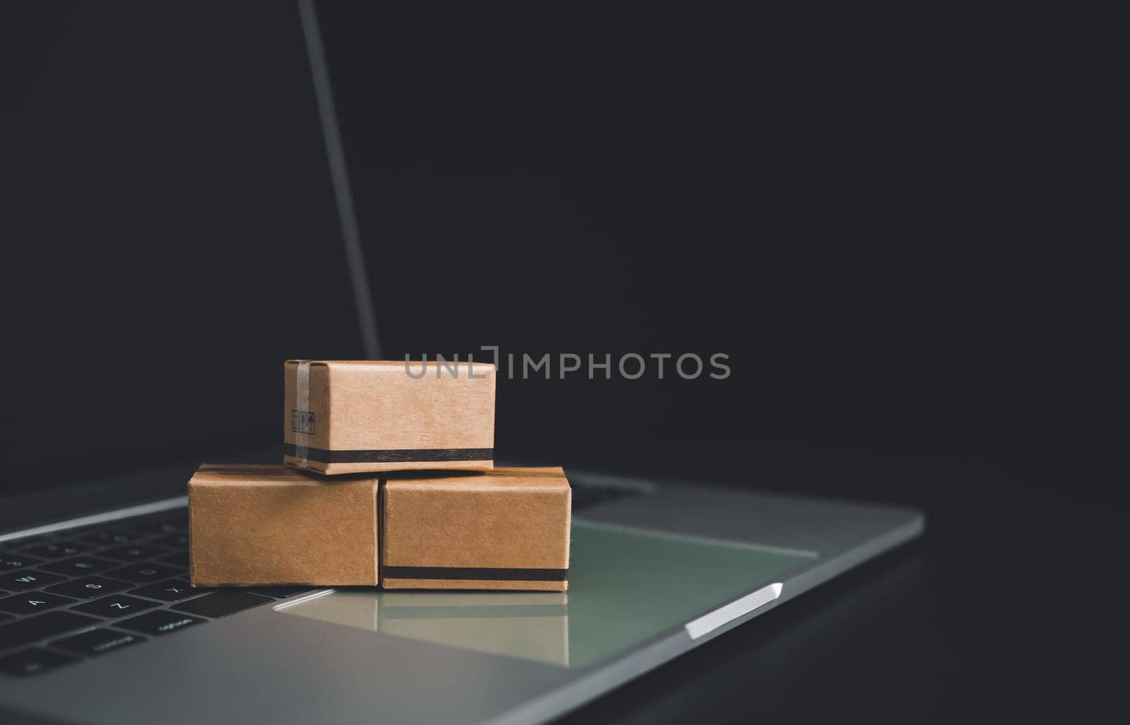 Boxes on a laptop keyboard on dark background. Ideas about online shopping, online shopping is a form of electronic commerce that allows consumers to directly buy goods from seller over the internet. by Unimages2527