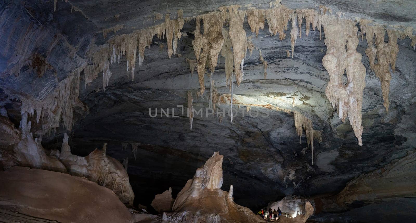 Anonymous tourists explore a large cave, lit by handheld lanterns that highlight its geological features.