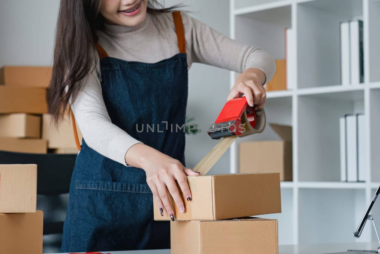 Young asian woman taping up a cardboard box in home office SME e-commerce business, relocation and new small business concept, SME concept.