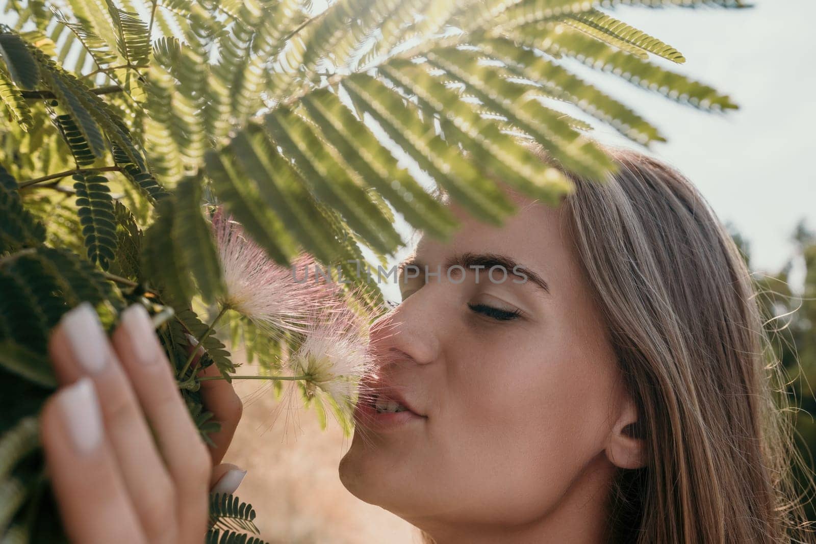 Beauty portrait of happy woman closeup. Young girl smelling Chinese acacia pink blossoming flowers. Portrait of young woman in blooming spring, summer garden. Romantic vibe. Female and nature by panophotograph