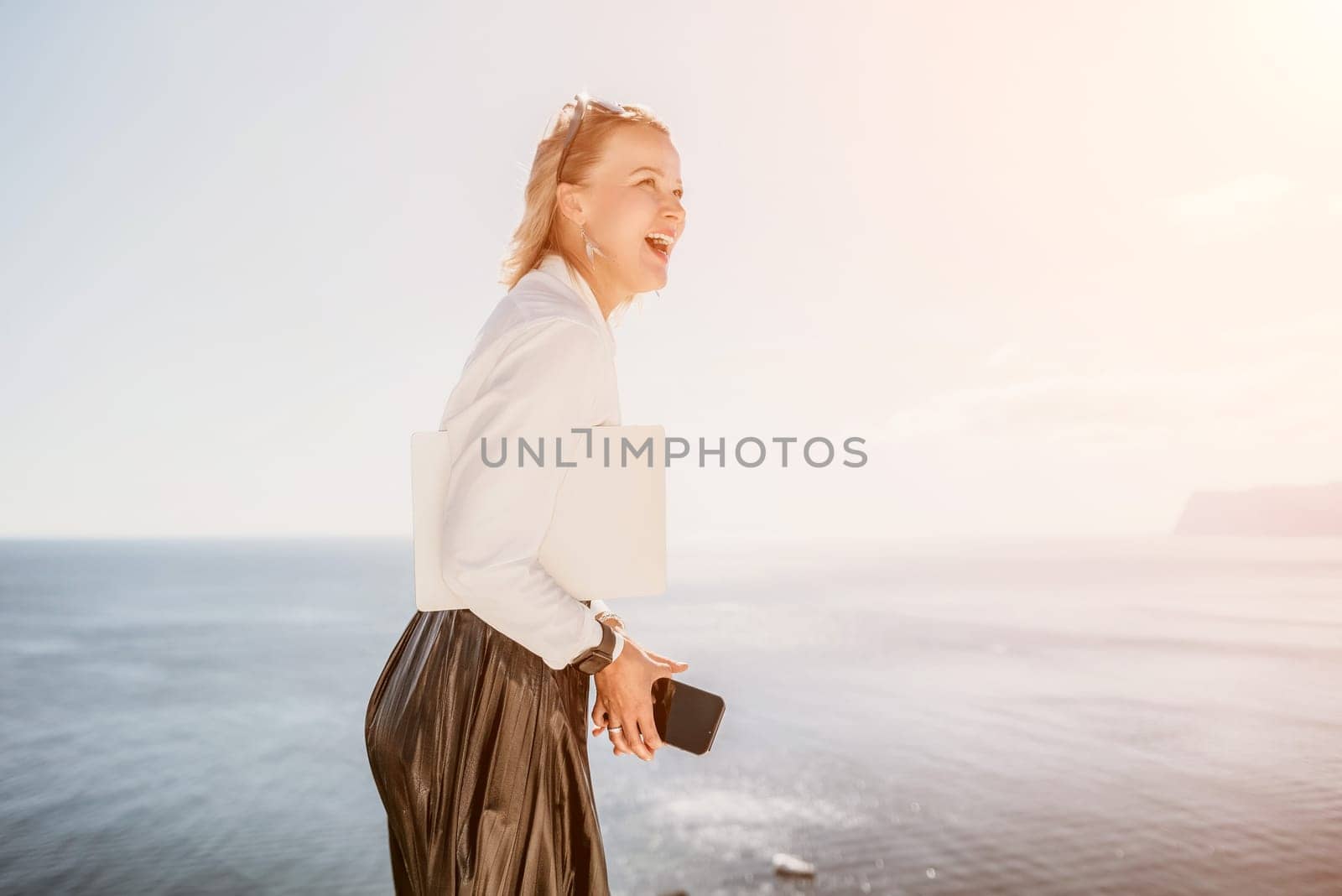 Digital nomad, Business woman working on laptop by the sea. Pretty lady typing on computer by the sea at sunset, makes a business transaction online from a distance. Freelance, remote work on vacation by panophotograph