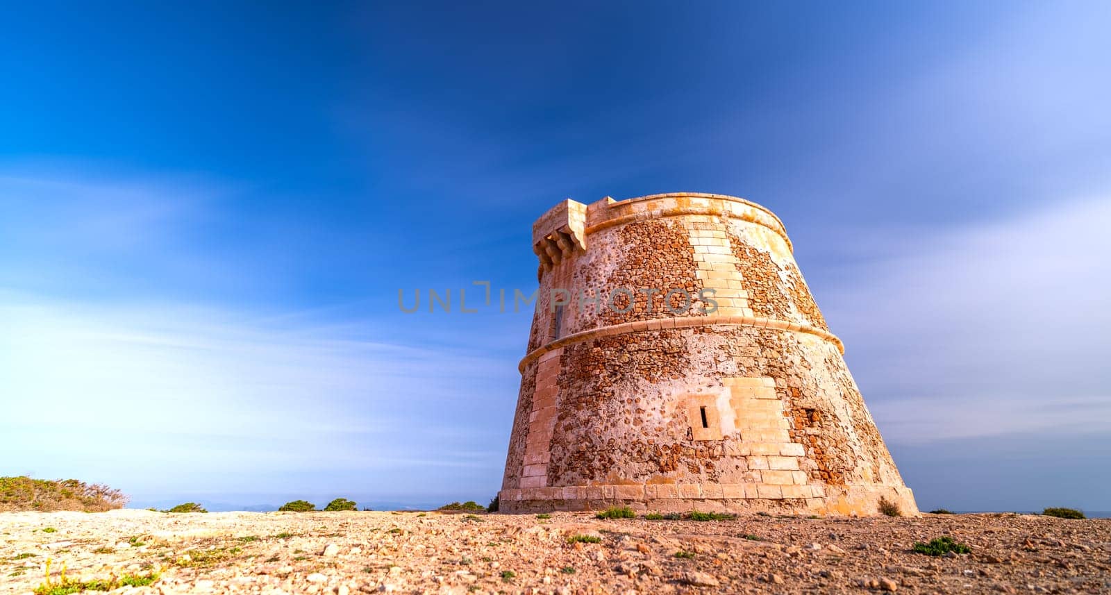 Ancient tower captured in long exposure under a silky cloud sky, brightly illuminated by the sun.