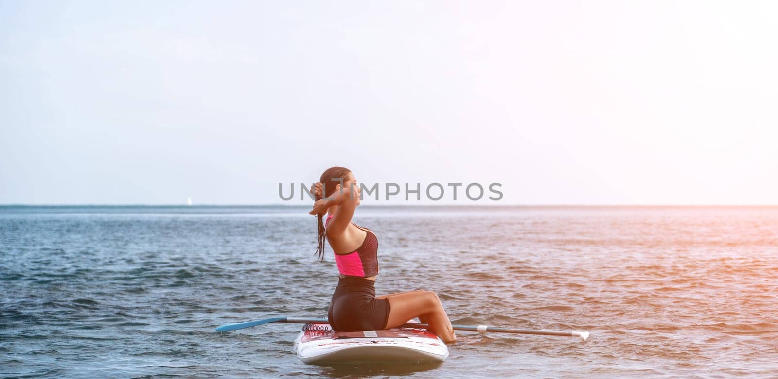 Sea woman sup. Silhouette of happy young woman in pink bikini, surfing on SUP board, confident paddling through water surface. Idyllic sunset. Active lifestyle at sea or river by panophotograph