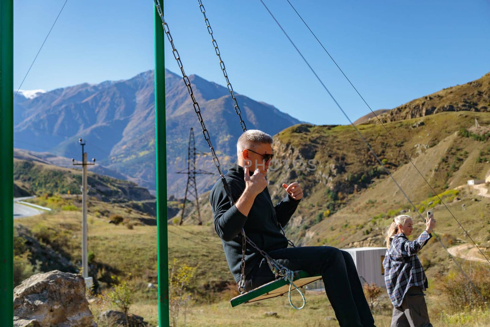 Man enjoying swinging on swing surrounded by mountains and beautiful natural landscape