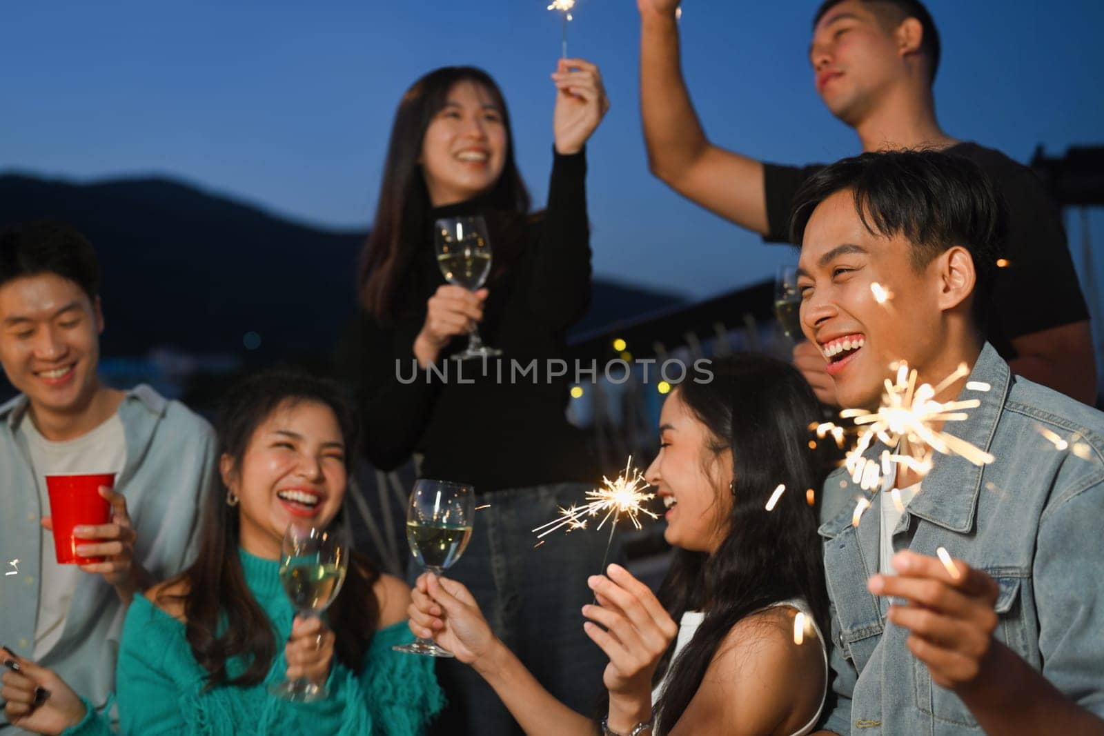 Group of young adult friends having fun a party on the rooftop with sparklers during sunset.