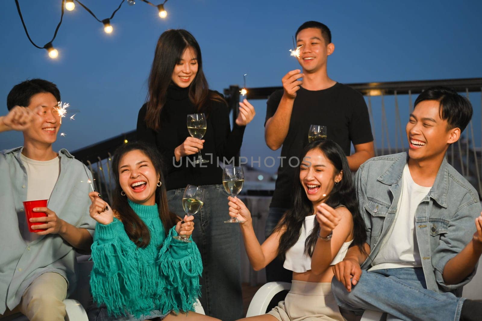 Group of young adult friends laughing and having fun at rooftop party. Friendship lifestyle concept.