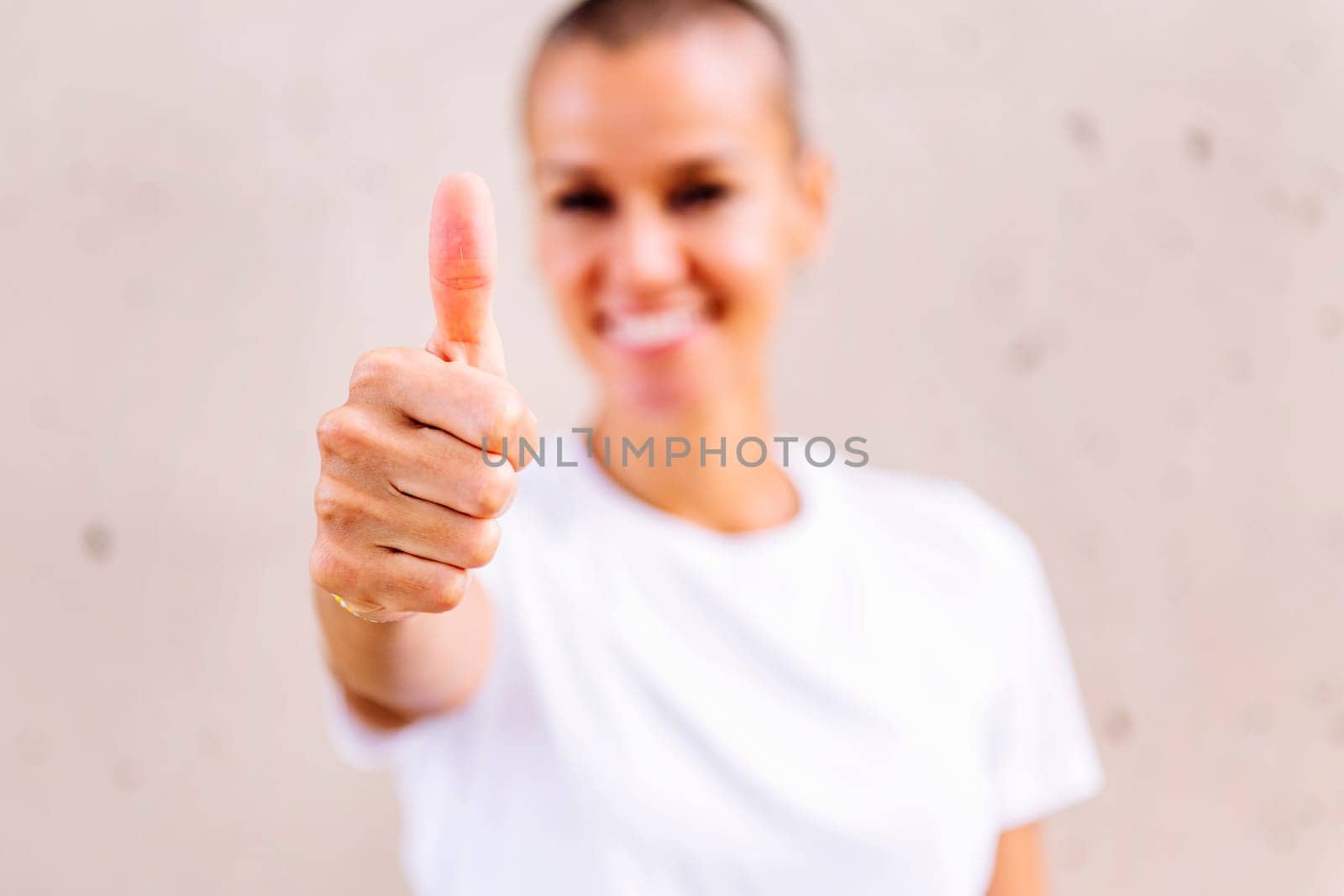 young woman with short hair smiling happy with with thumb up looking at camera, focus on hand, copy space for text