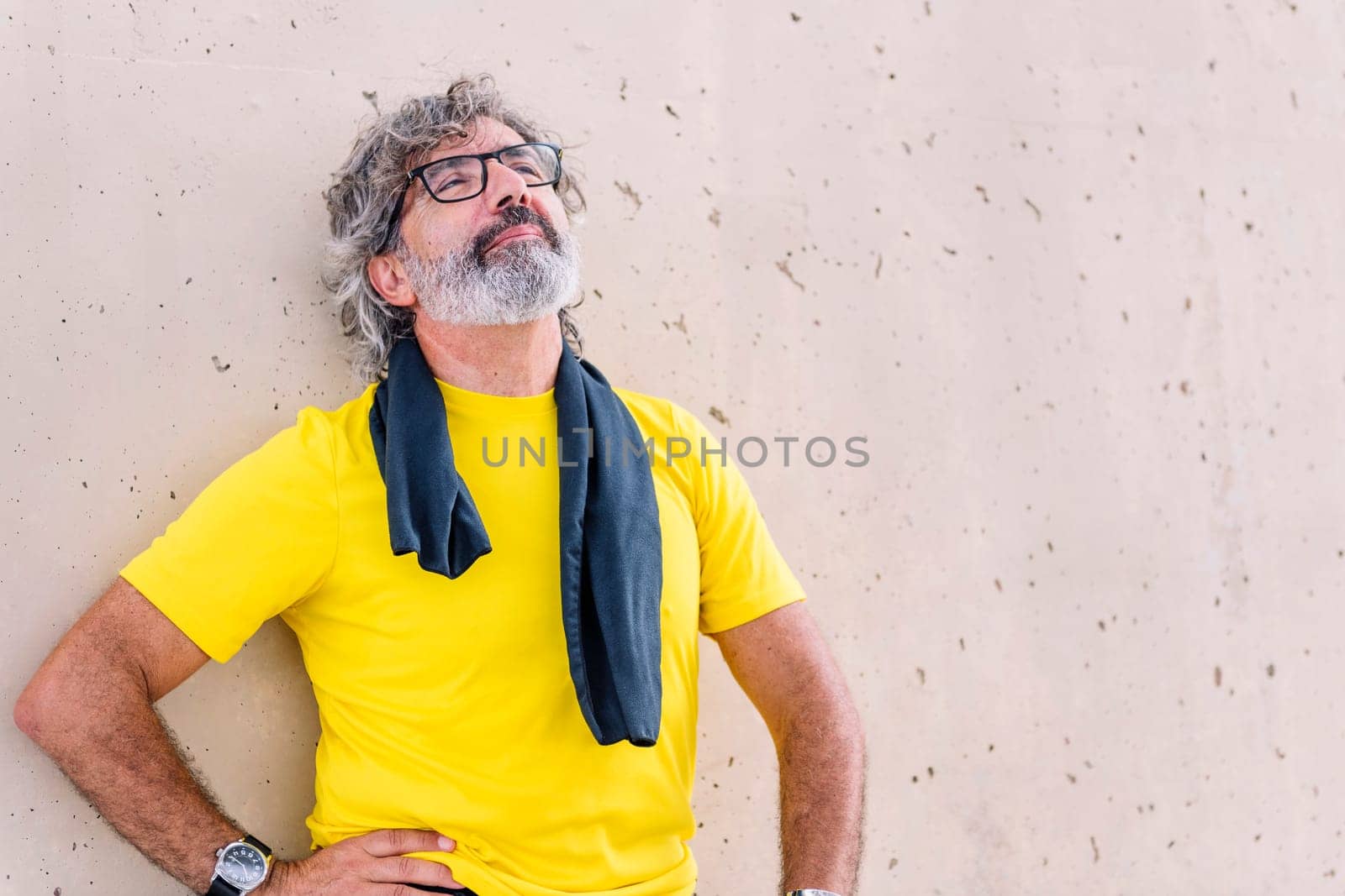 senior sports man with glasses resting leaning on a wall, concept of active and healthy lifestyle on the middle age, copy space for text