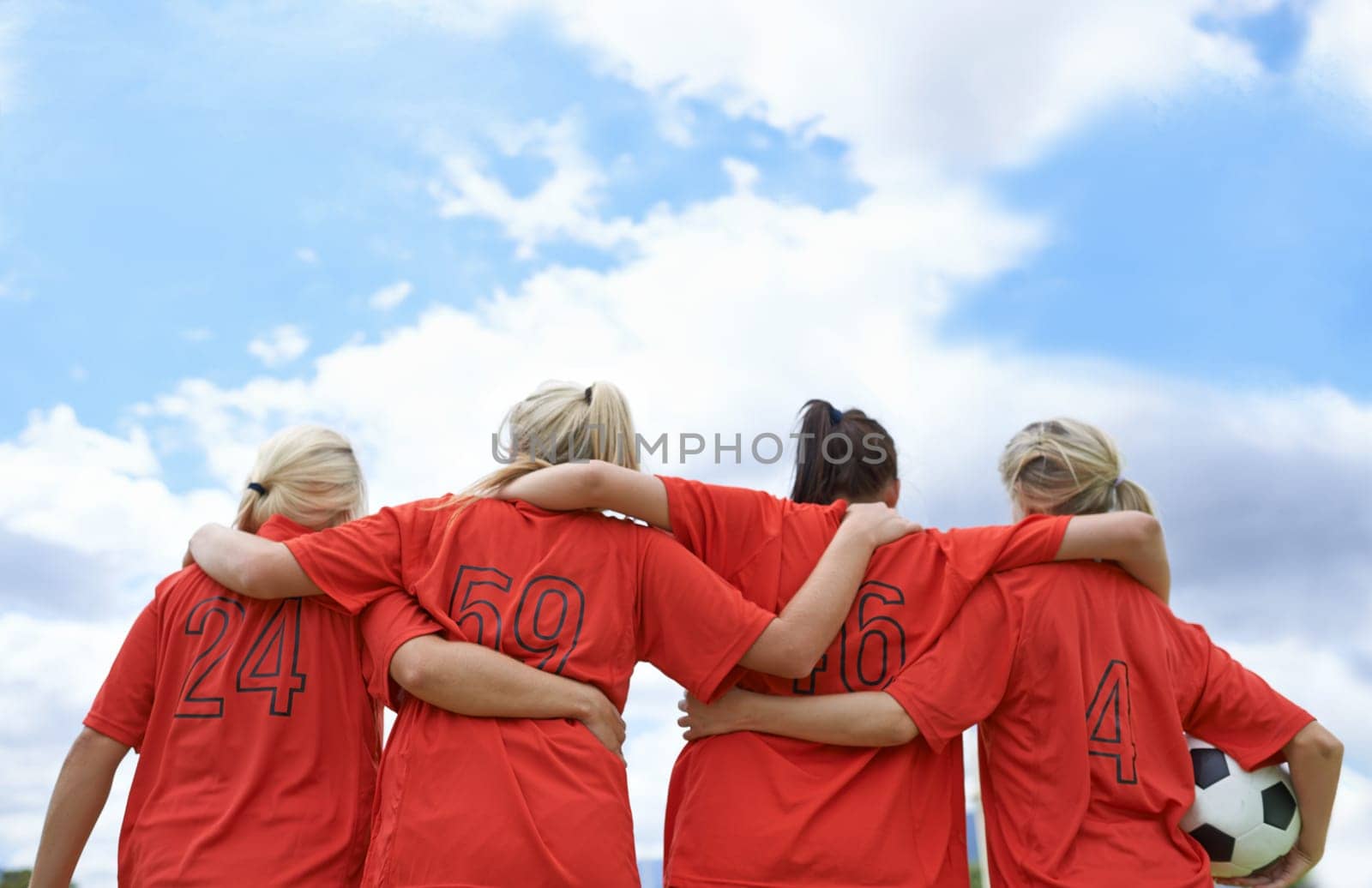 Woman, hug and back of soccer team ready for sports match, game or outdoor practice with blue sky. Rear view of female person or group of football players standing in unity with ball in nature by YuriArcurs