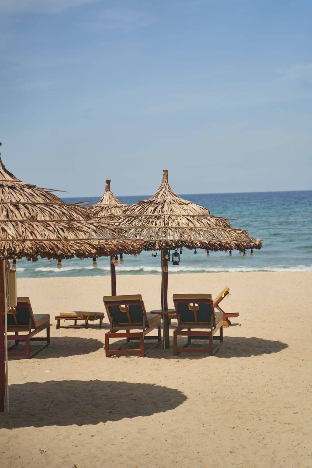 Straw sunshades and sunbeds on the empty pebble beach with sea in the background. Deserted beach with rattan sun loungers and umbrellas