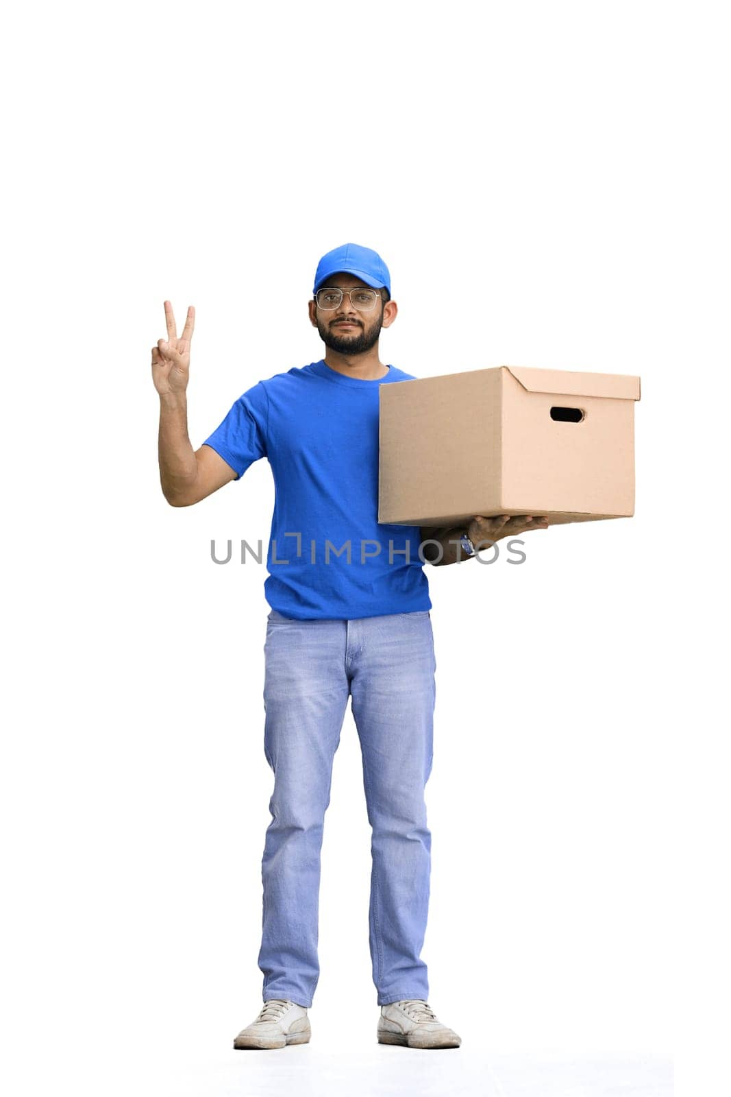 A male deliveryman, on a white background, in full height, with a box, shows a victory sign.