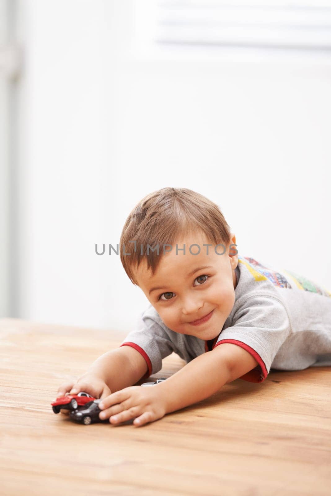 Cars, toys and portrait of child by table playing for learning, development and fun at modern home. Cute, sweet and boy kid enjoying a game with plastic vehicles by wood for childhood hobby at house