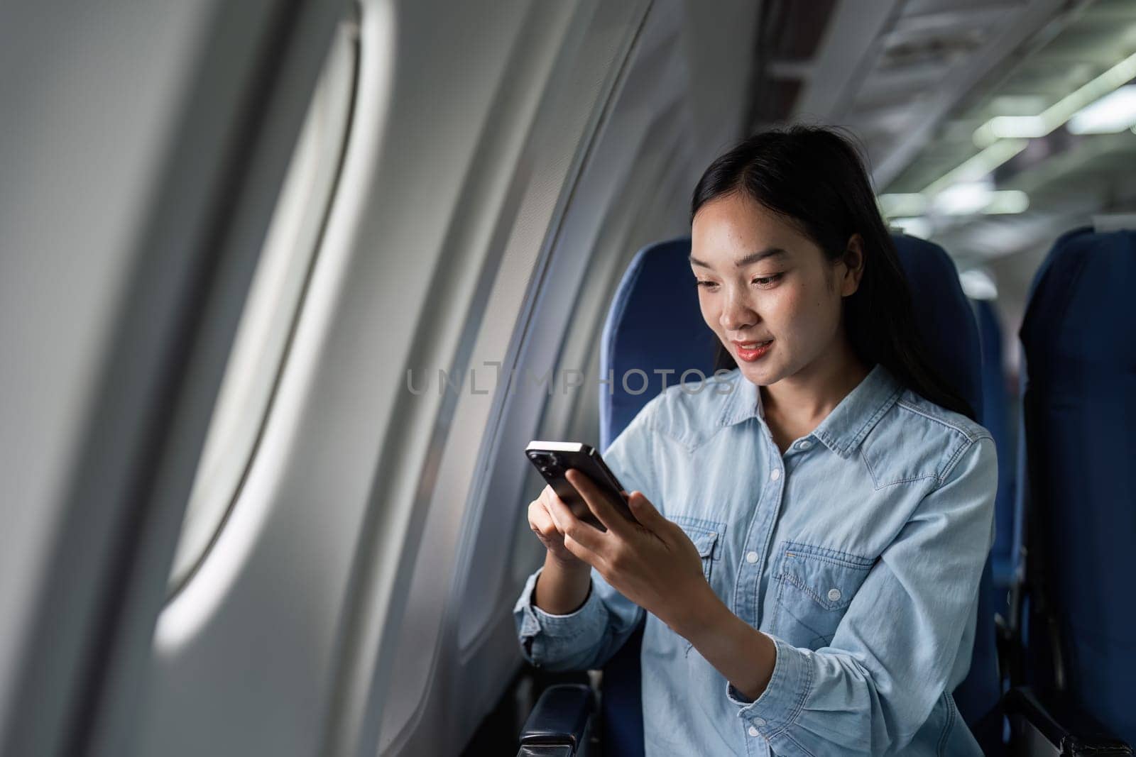 Asian people female person onboard, airplane window, using mobile while on the plane.