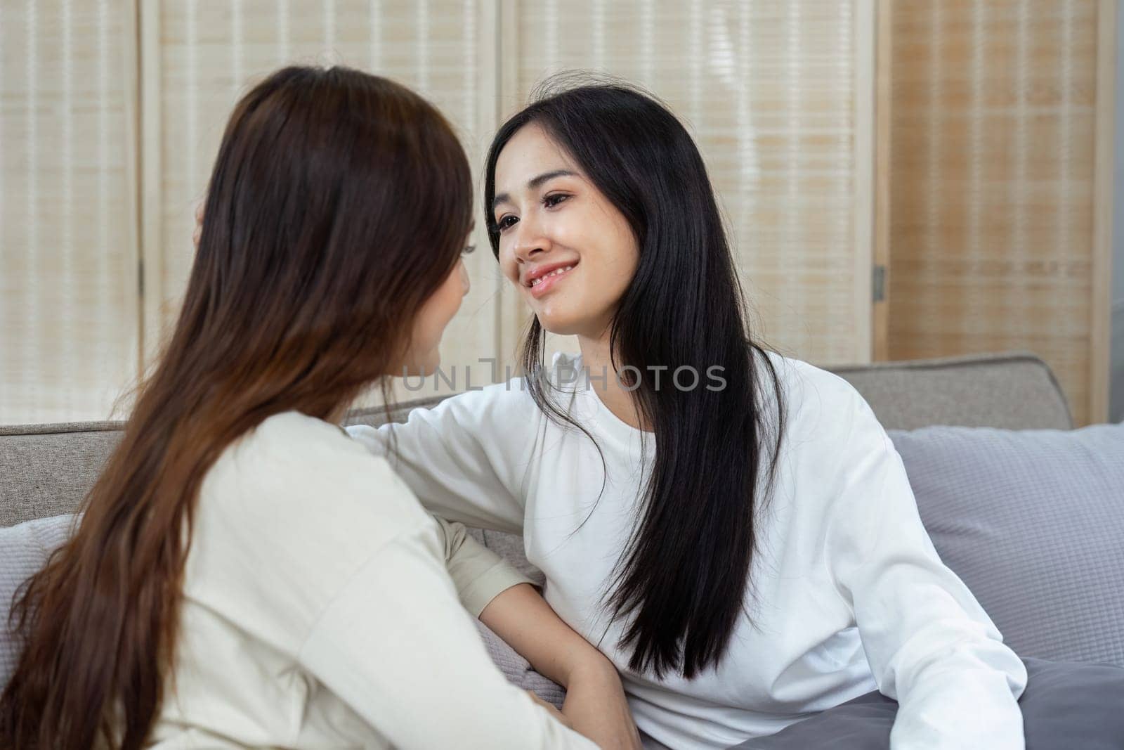 Happy lesbian young Asian couple spending weekend together, resting on couch at home.
