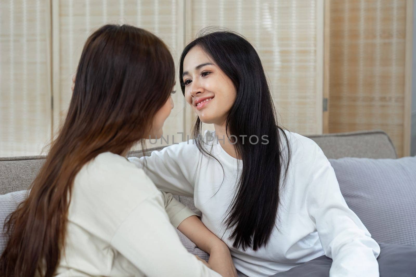 Happy lesbian young Asian couple spending weekend together, resting on couch at home by itchaznong