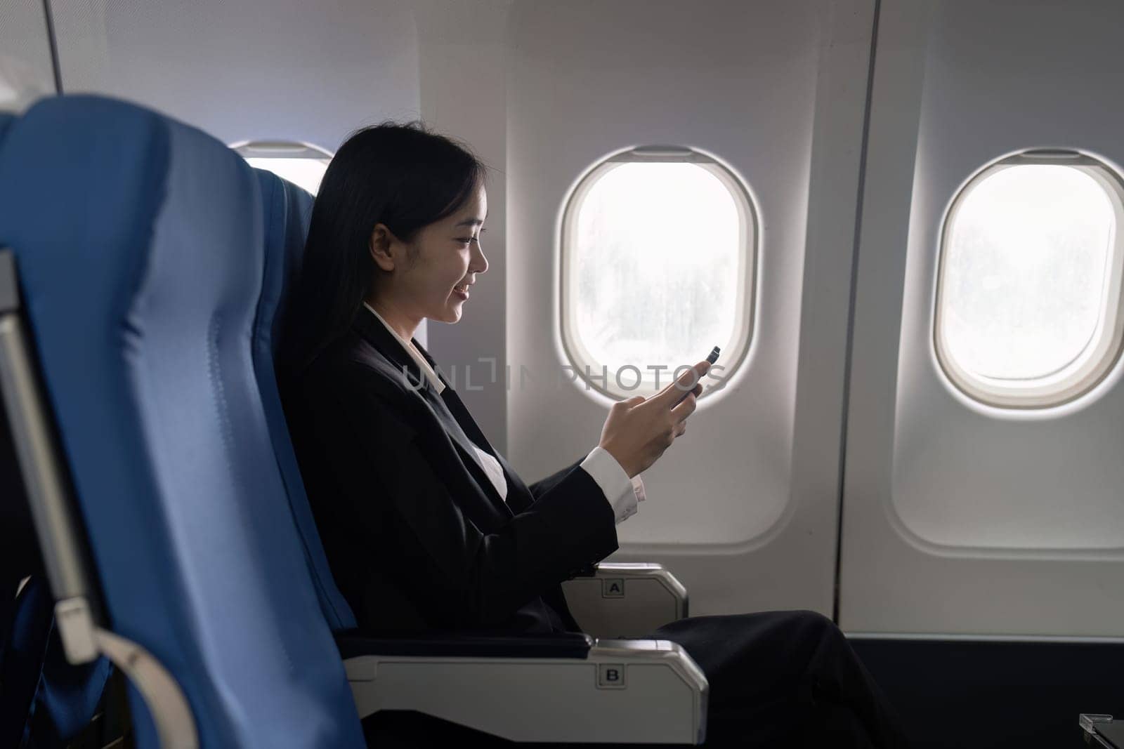 businesswoman flying and working in an airplane in first class, sitting inside an airplane using mobile.