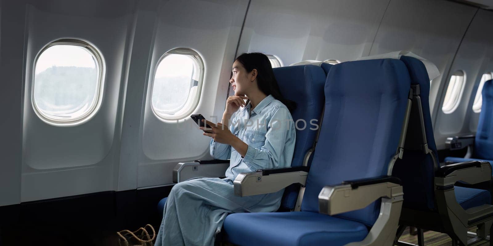 Asian people female person onboard, airplane window, using mobile while on the plane.