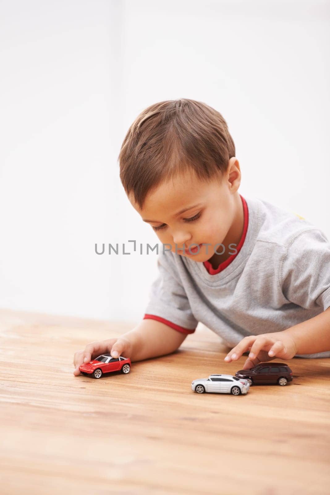 Cars, toys and boy child by table playing for learning, development and fun at modern home. Cute, sweet and young kid enjoying a game with plastic vehicles by wood for childhood hobby at house