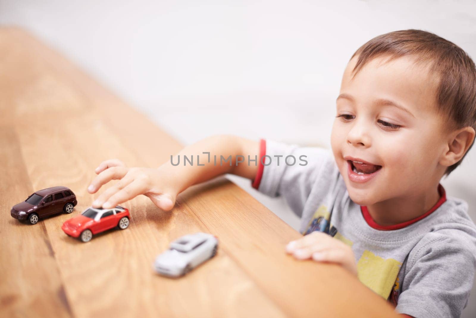 Cars, toys and boy kid by table playing for learning, development and fun at modern home. Cute, sweet and young child enjoying a game with plastic vehicles by wood for childhood hobby at house