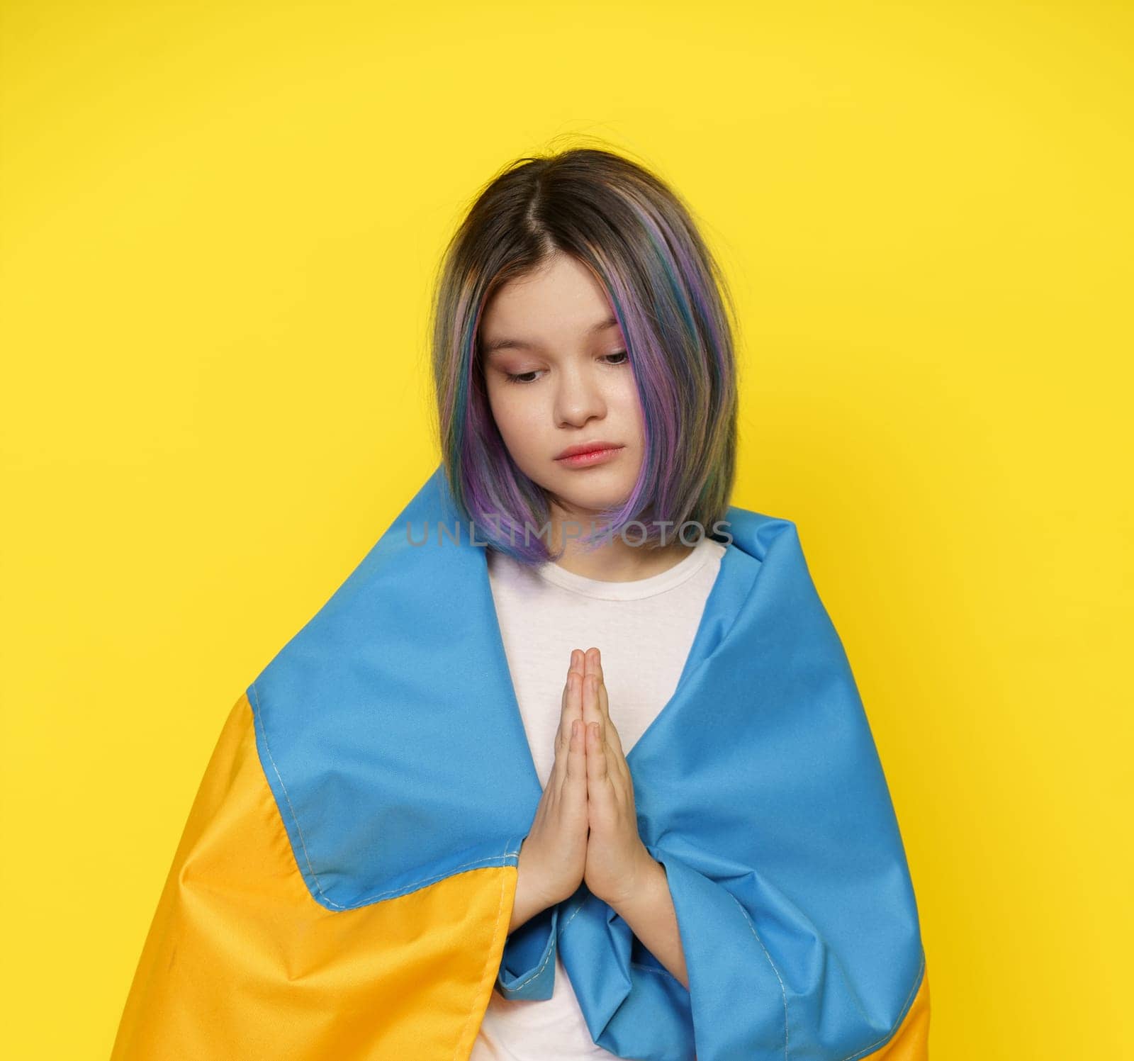 Girl Covers Herself With The Ukrainian Flag And Prays For Quick Peace Agreement In Ukraine, Amidst Ongoing Conflict With Russia. Symbol Of Global Awareness And Support For Those Affected By Crisis In Ukraine. High quality photo