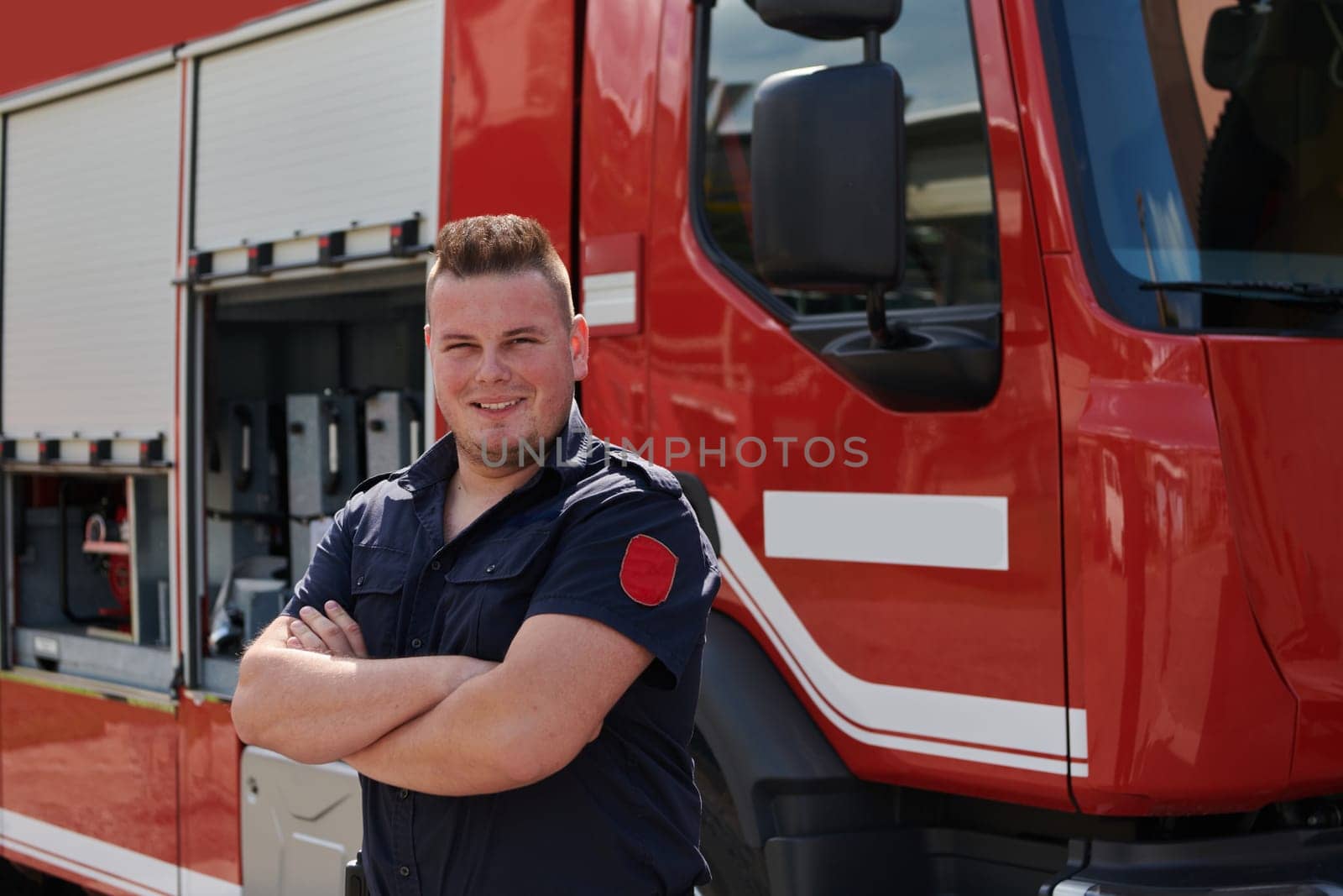 Confident firefighter stands with crossed arms, exuding resilience and preparedness, ready to respond to emergencies alongside a modern fire truck, showcasing the heroism and strength of the fire service by dotshock