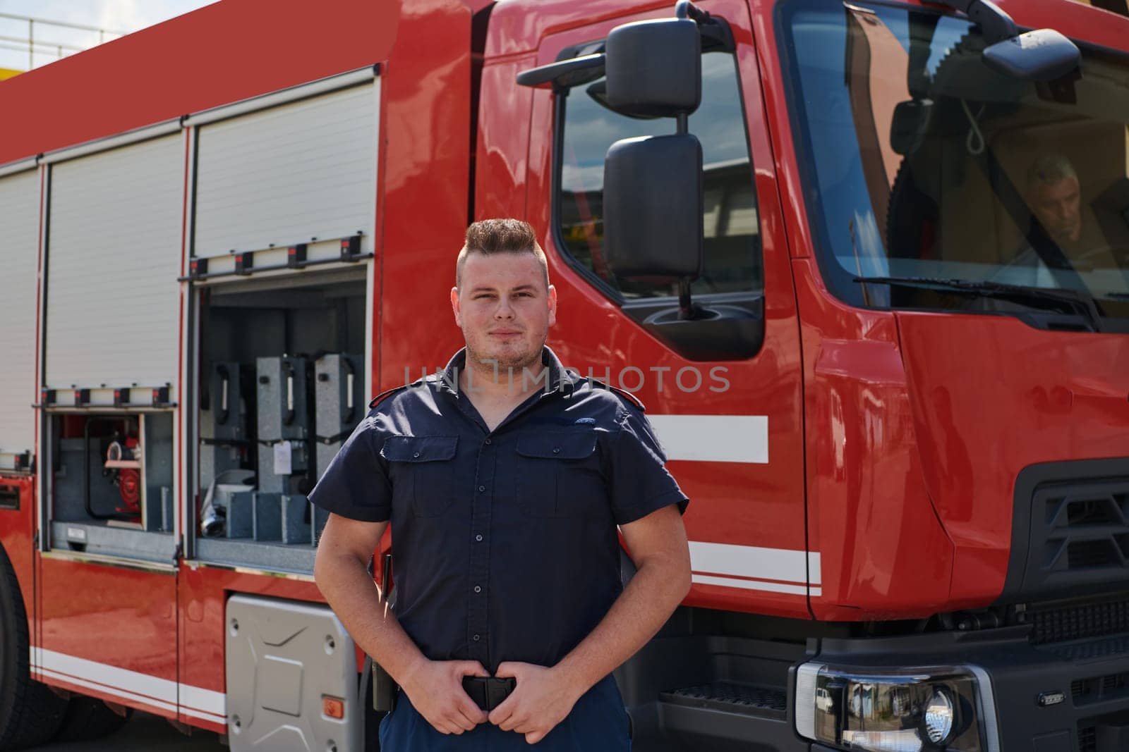 A confident firefighter strikes a pose in front of a modern firetruck, exuding pride, strength, and preparedness for emergency response.