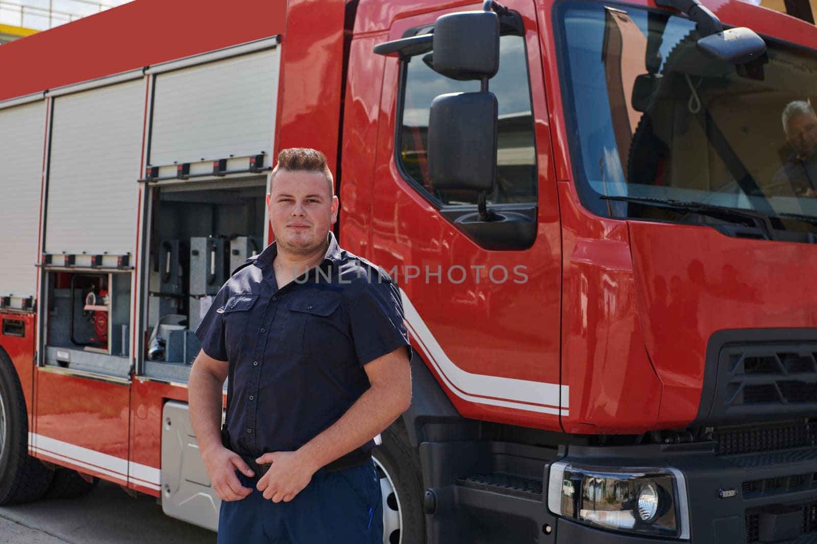 A confident firefighter strikes a pose in front of a modern firetruck, exuding pride, strength, and preparedness for emergency response by dotshock