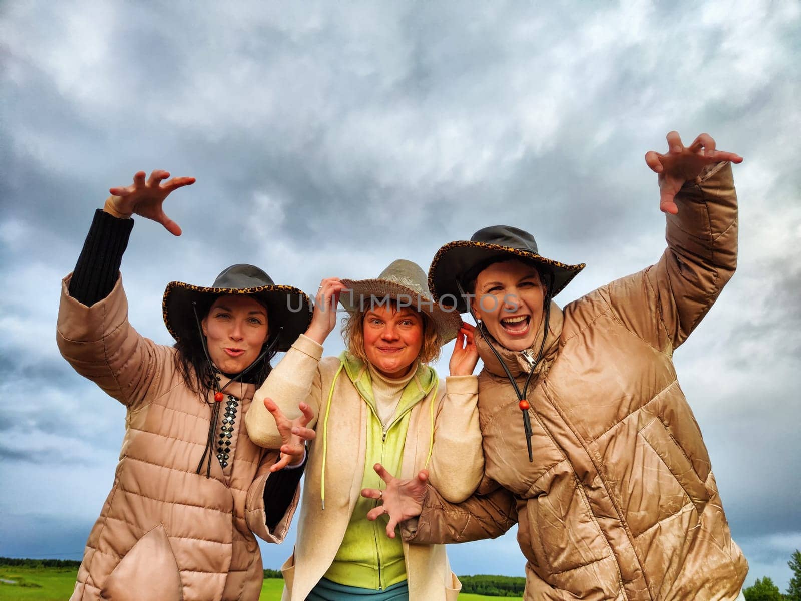 Adult girls looking like a cowboys in hats in a field and with a stormy sky with clouds posing in the rain. Women having fun outdoors on rural and rustic nature