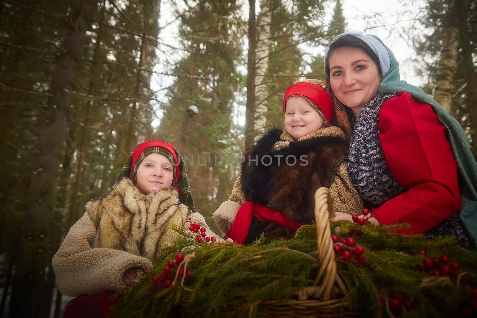 Family with mother, teenage girl, and little daughter dressed in stylized medieval peasant clothing in winter forest. Woman and her daughters pose for fairytale photoshoot in nature on a cold day