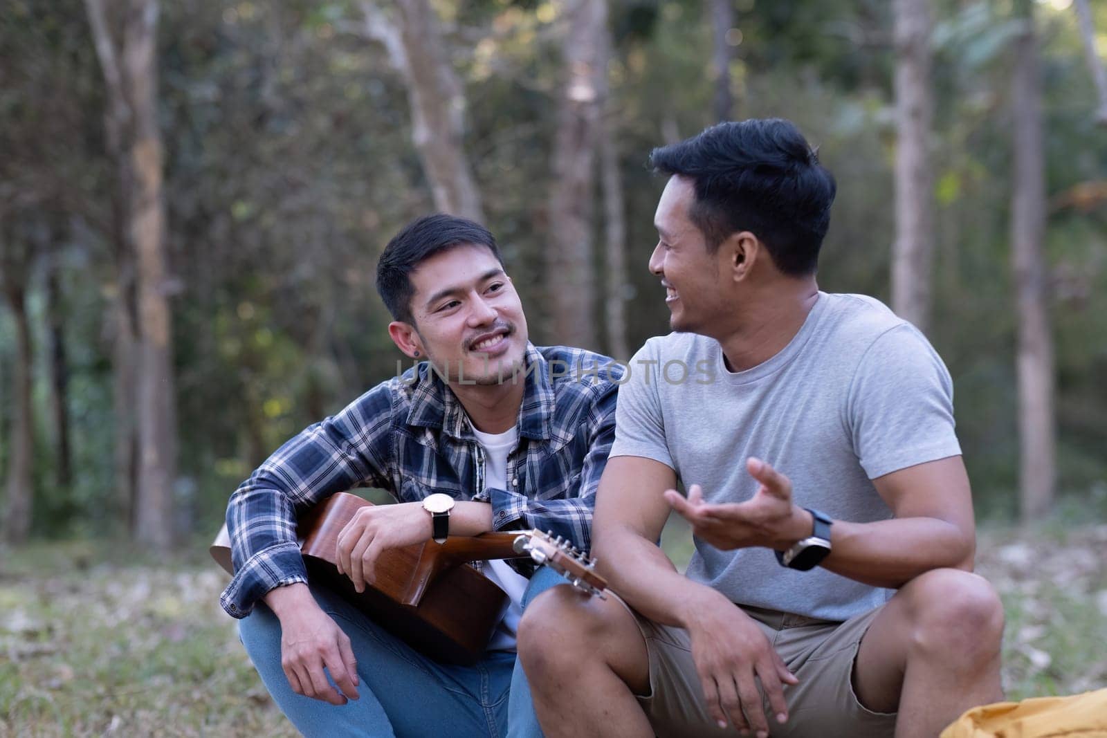 Asian LGBTQ couple enjoying nature, camping with tents in the forest area by the river, playing guitar. by wichayada