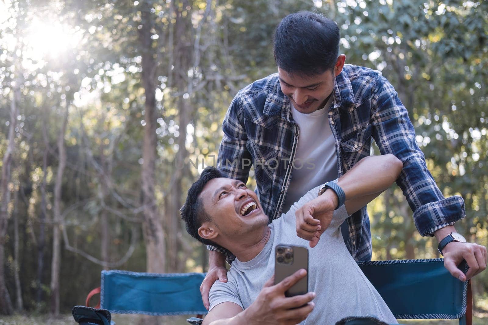 Asian LGBTQ couple tent in front of camp talking on smartphone in video chat or take a selfie.