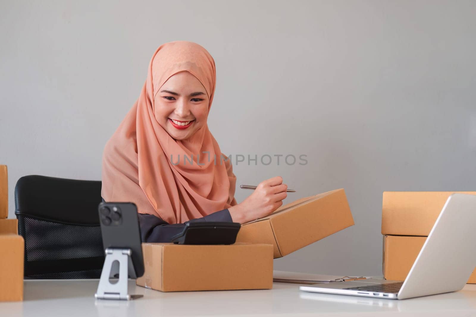 Asian Muslim businesswoman checks stock orders and saves them on her home office laptop. small business owner Shipping in online markets The concept of freedom in life.