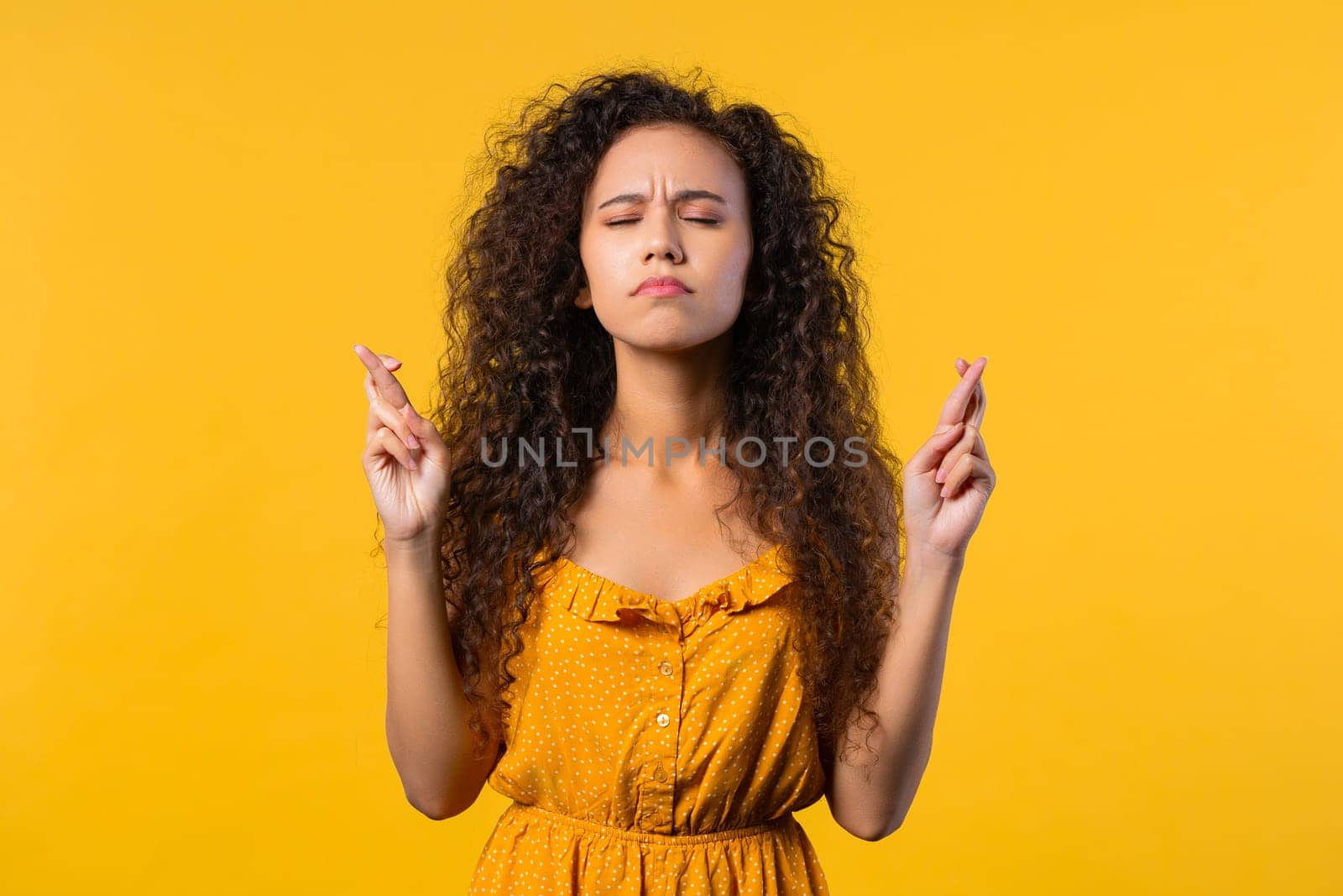 Student praying with crossed fingers on yellow background. Woman begs someone satisfy desires, help with, prays for luck in exam. High quality